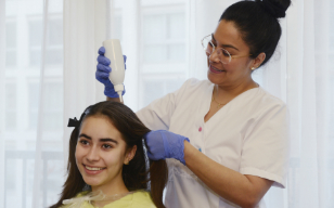 Professionnelle utilisant un appareil de traitement sur les cheveux d'une jeune fille pour un soin anti-poux.